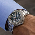 Oris Aquis Date Upcycle Herenhorloge 41,5mm met kleurrijke wijzerplaat en roestvrijstalen band, gedragen om een pols met blauw overhemd. Ideaal voor duurzame stijl.