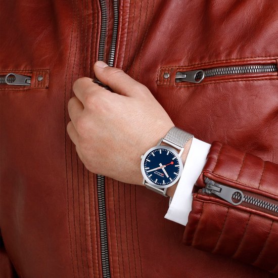 Mondaine Classic Spoorweg Horloge 40mm M660.30360.40SBJ heren horloge met blauwe wijzerplaat en mesh band, gedragen bij roodleren jas. Swiss Made design.