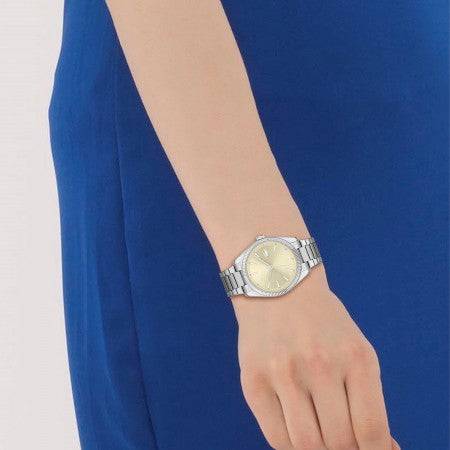 Lacoste Dameshorloge 36mm LC2001239 met zilverkleurige band en goudkleurige wijzerplaat, gedragen om een pols met blauwe jurk.
