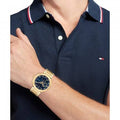 Tommy Hilfiger TH1792118 LORENZO Herenhorloge 44mm met goudkleurige band en blauwe wijzerplaat, gedragen bij navy poloshirt. Stijlvol accessoire voor herenmode.