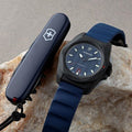 Victorinox I.N.O.X. herenhorloge 242022.1 met blauwe rubberen band en 43mm kast, naast een Zwitsers zakmes op een steen. Swiss Made duikhorloge met 20 ATM waterdichtheid.